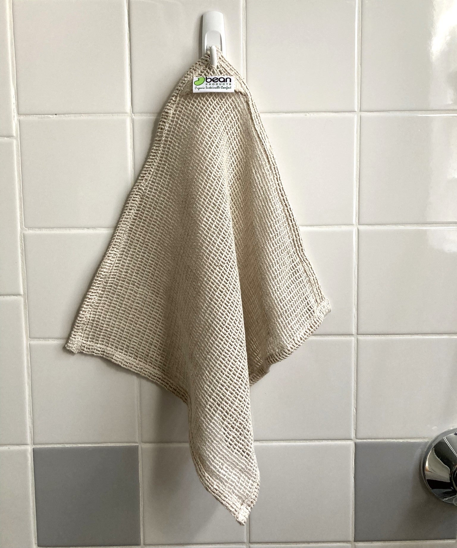 Beige dishcloth hanging on a hook against a tiled wall