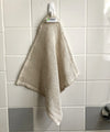 Beige dishcloth hanging on a hook against a tiled wall