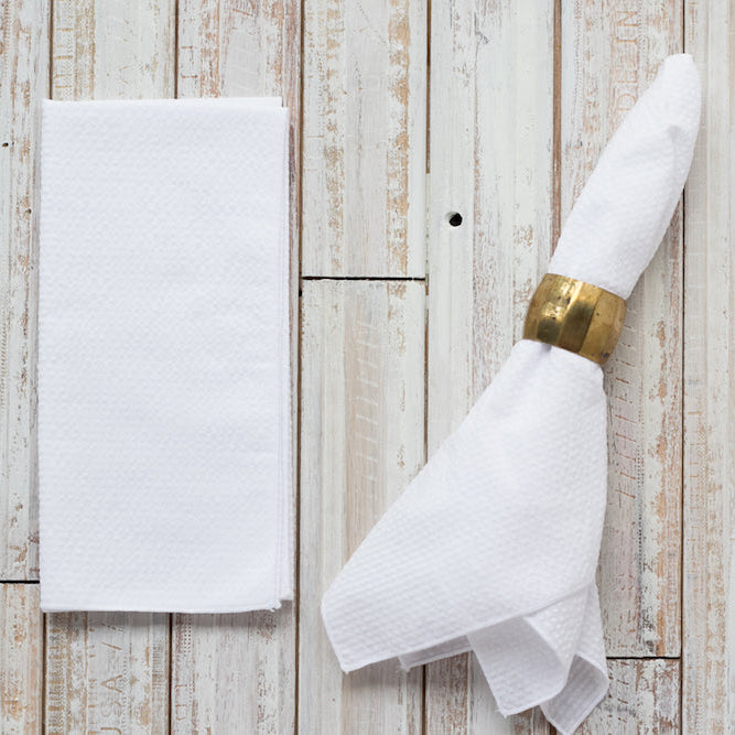White napkin with a gold napkin ring on a wooden surface