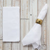 White napkin with a gold napkin ring on a wooden surface