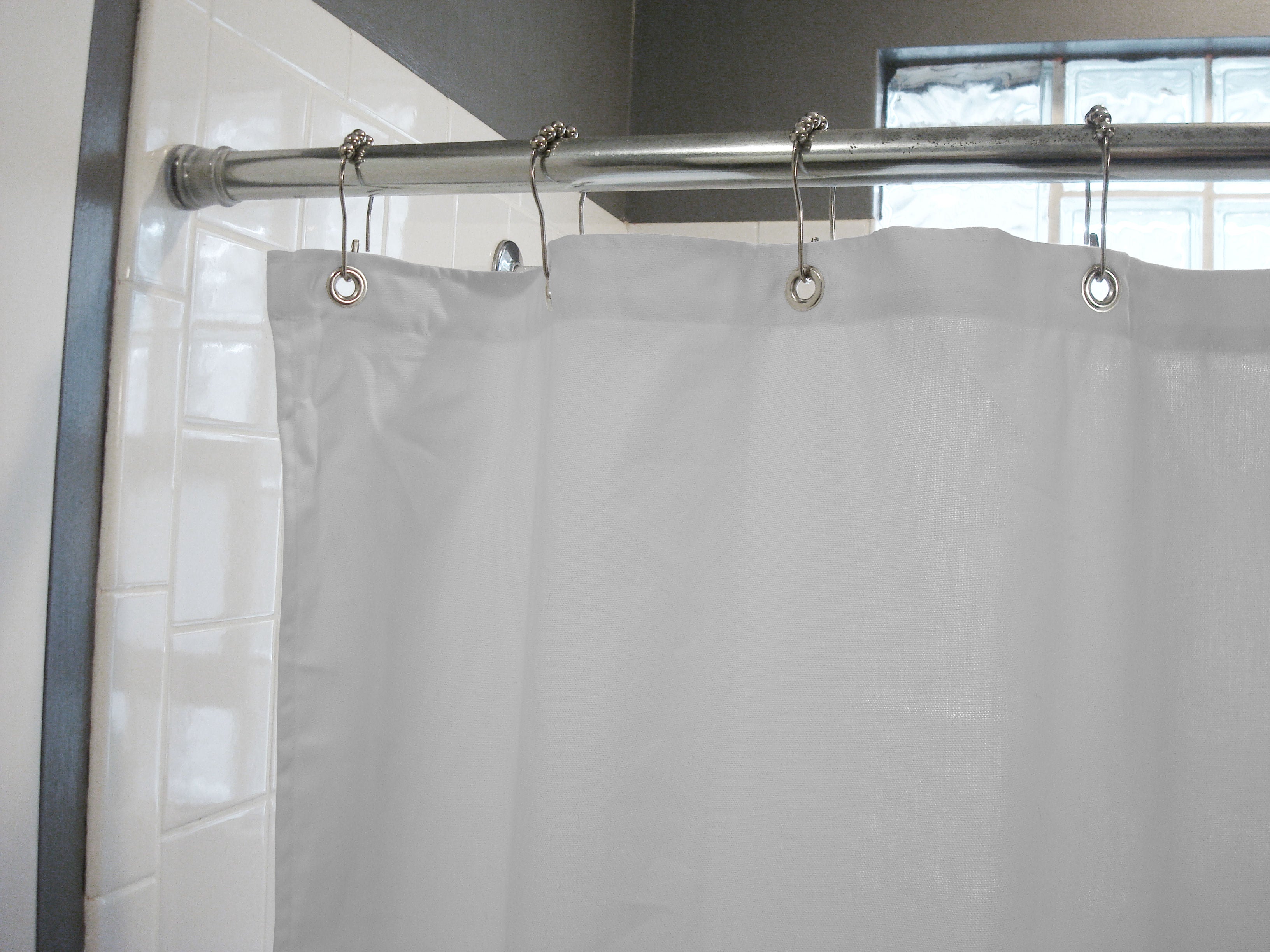 White shower curtain with silver hooks on a rod in a bathroom setting.