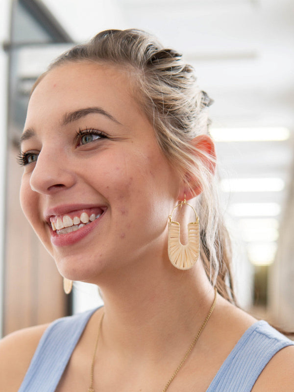 Close-up of white woven loop earrings by Fair Anita showing raffia texture and brass detail