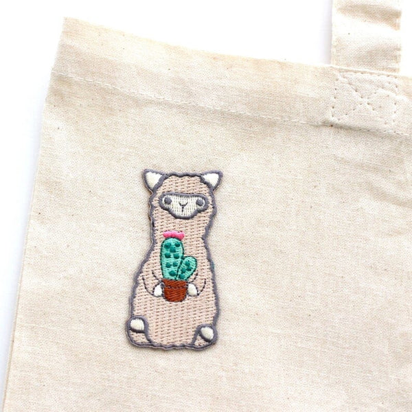 Embroidered llama holding a cactus on a beige fabric background