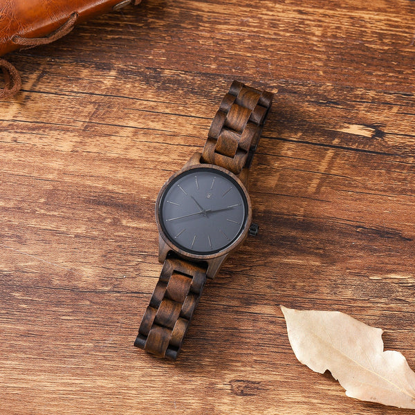 Wooden watch with dark face on a wooden surface with a leaf
