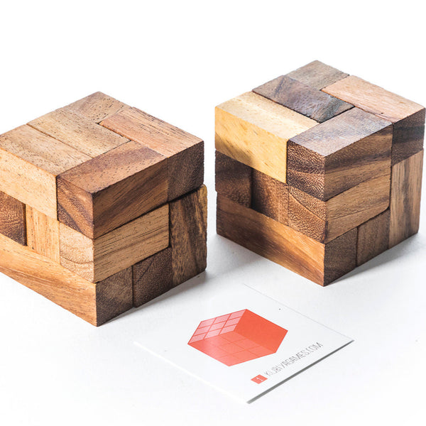 Two wooden puzzle cubes on a white surface with a small red and white card.