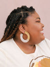 Close-up of woven metallic hoop earrings showing natural fiber texture and colorblock pattern