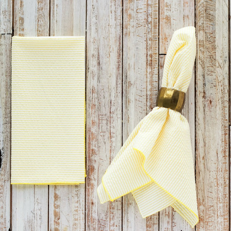 Yellow napkin with a gold napkin ring on a wooden surface