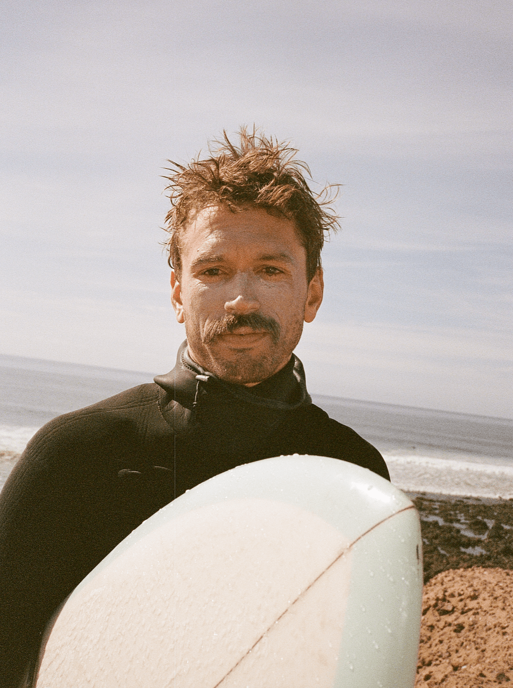 Man in a wetsuit holding a surfboard on a beach