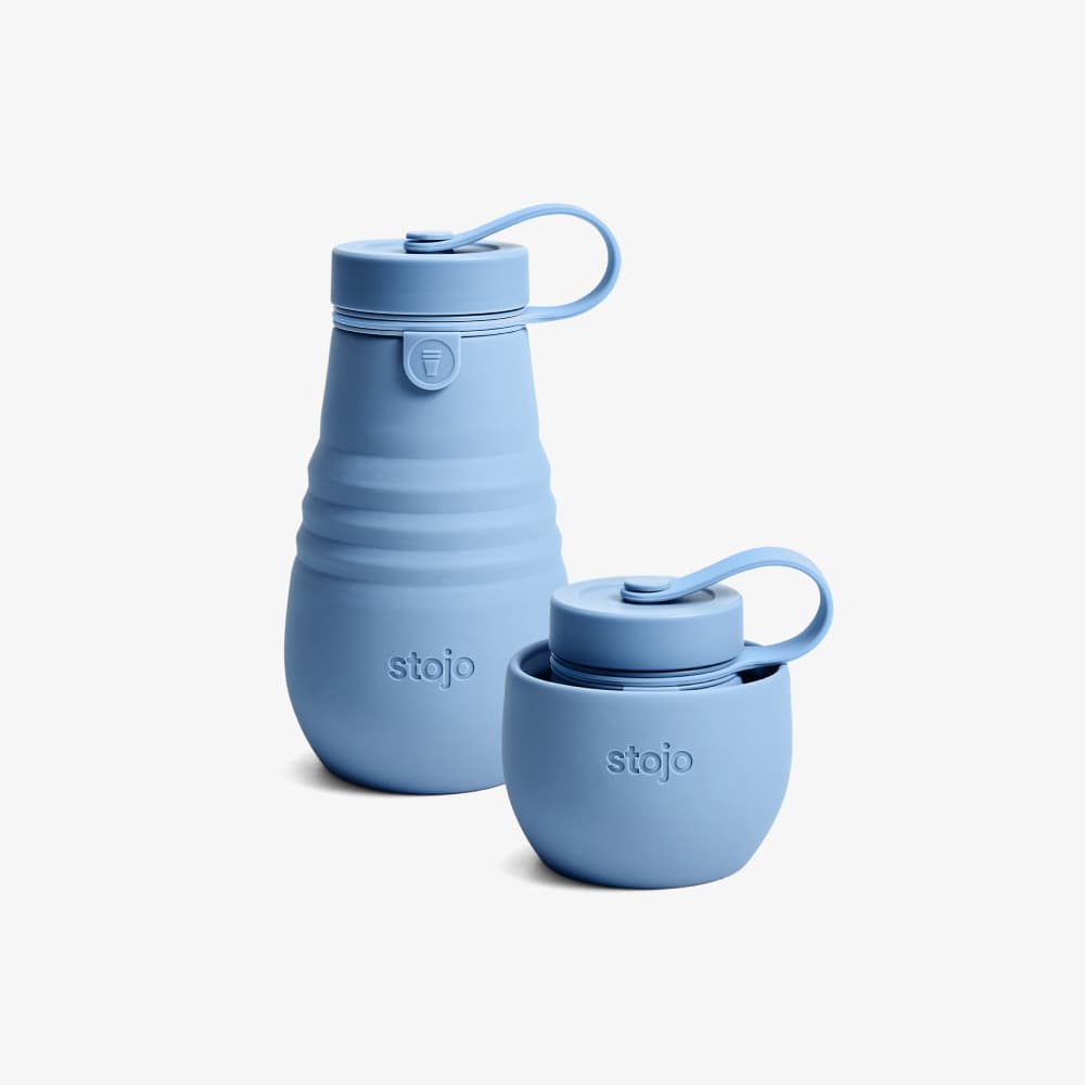 A blue collapsible water bottle made by Stojo. The bottle is made of silicone and has a blue silicone loop on the top. The bottle is collapsed in the picture, but it can be expanded to hold 14 ounces of water.