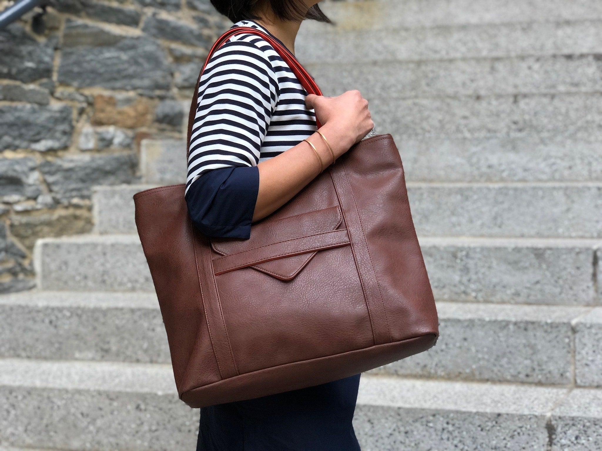 Person holding a brown leather tote bag on stone steps
