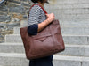 Person holding a brown leather tote bag on stone steps