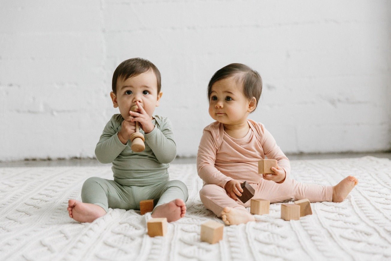 A baby holding a classic baby rattle made by Bannor Toys. The rattle is made of maple wood and has a natural beeswax and flaxseed oil finish. The baby is holding the rattle in their right hand and is looking at it with interest. The rattle is making a gentle noise as the baby shakes it.