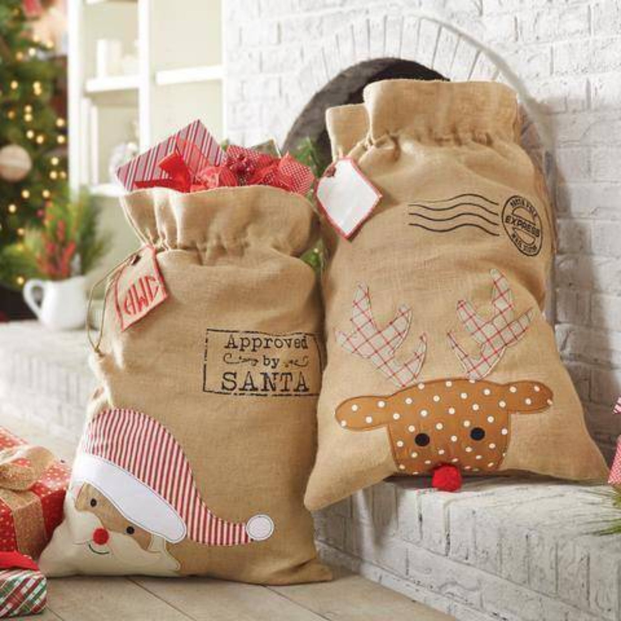 Two decorative Christmas sacks with festive designs on a white brick wall background.