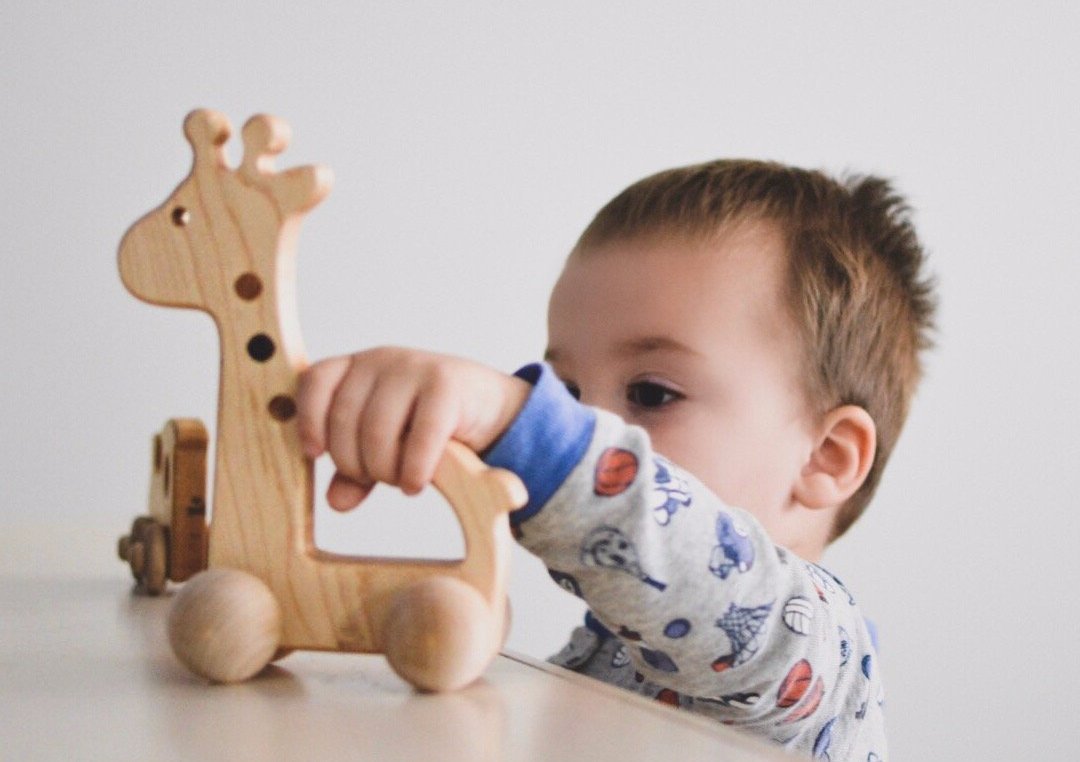 A photo of a child pushing a wooden giraffe push toy. The child is smiling and having fun.
