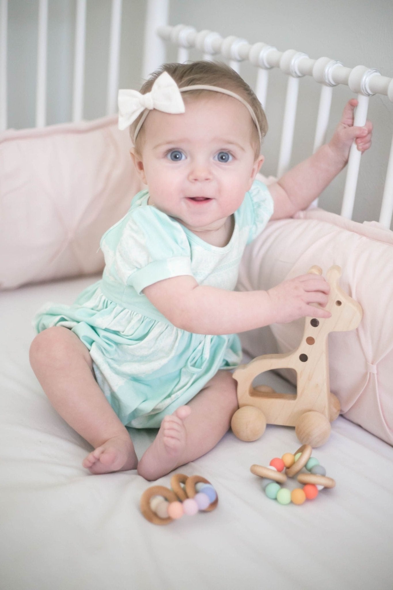 A photo of a baby pushing a wooden giraffe push toy. The baby is smiling and having fun.