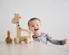 A photo of a wooden giraffe push toy. The giraffe is sitting on a wooden floor.